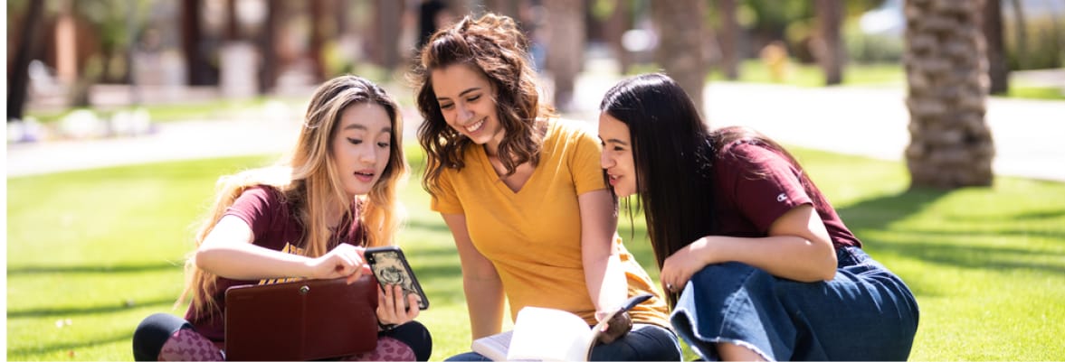 Three ASU women sitting on campus and looking at a phone