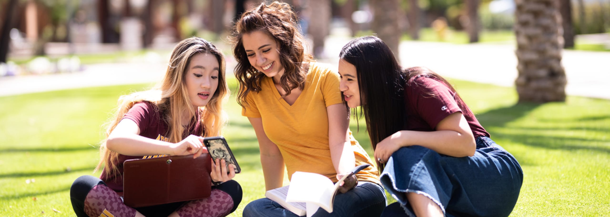 Three ASU students sitting on campus and looking at phone