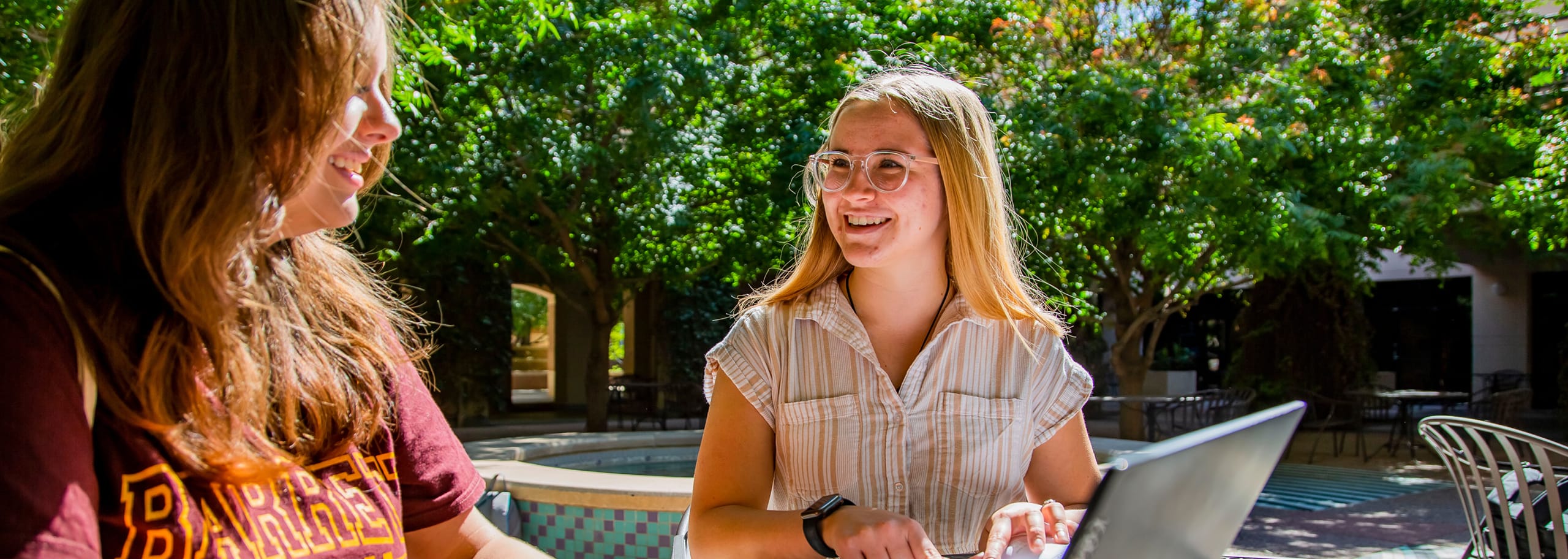 Two female students sitting outside and smiling