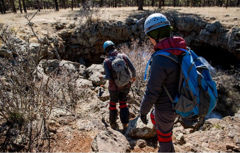 People walking around cave opening and studying rocks