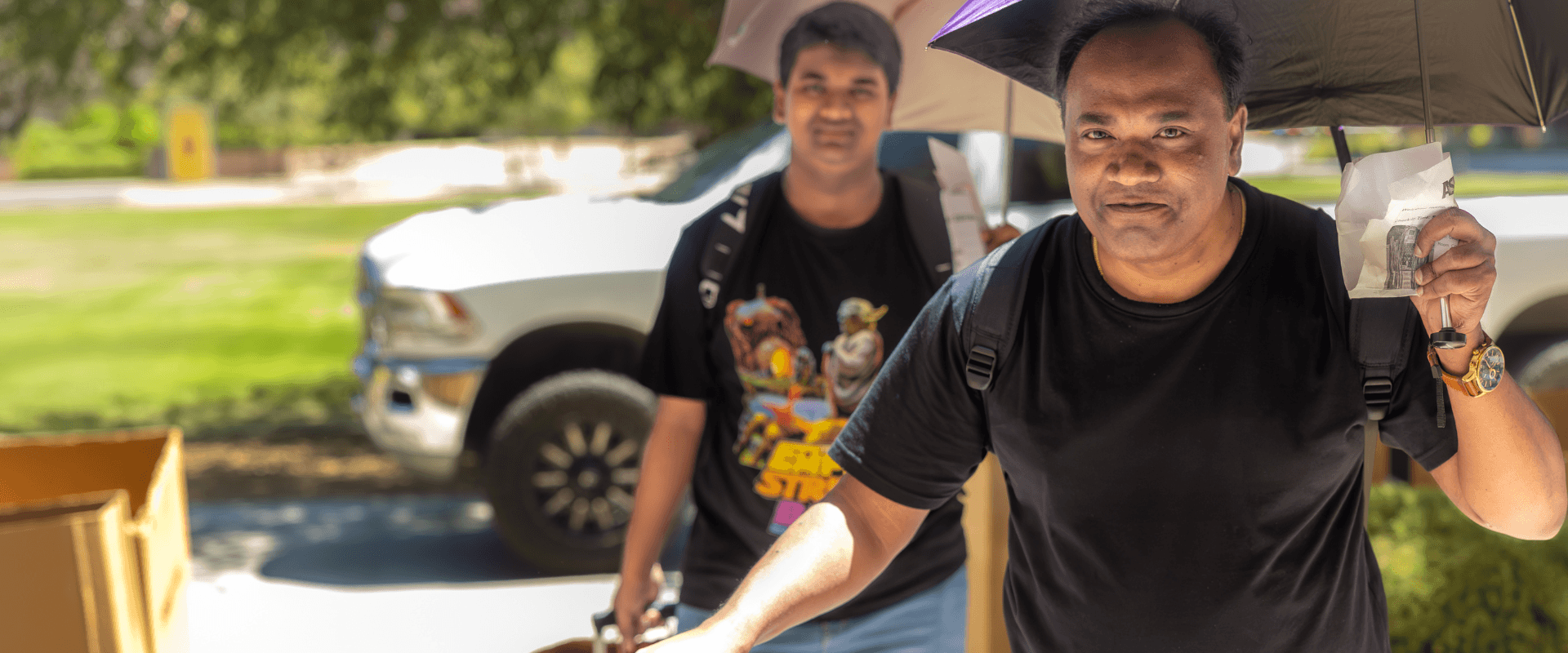 A father and son walking outdoors during college move-in day on a bright, sunny afternoon.